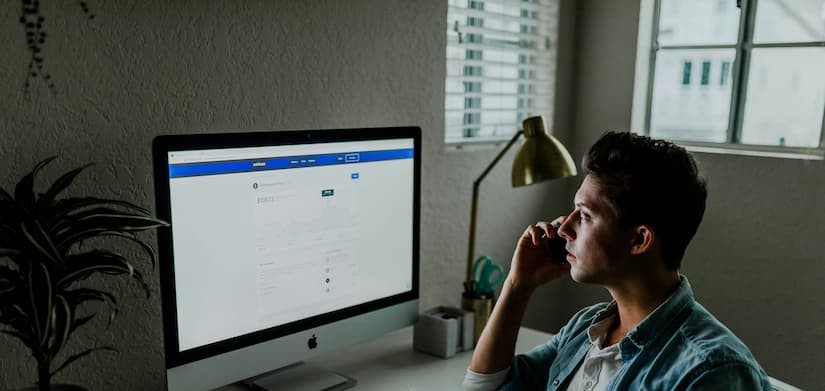 Homem sentado diante de um computador enquanto fala ao telefone desenvolvendo estratégia de retargeting.