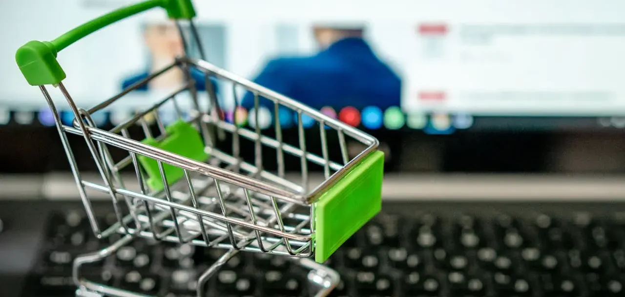 Imagem de um carrinho de compras em miniatura, apoiado em um teclado de notebook.