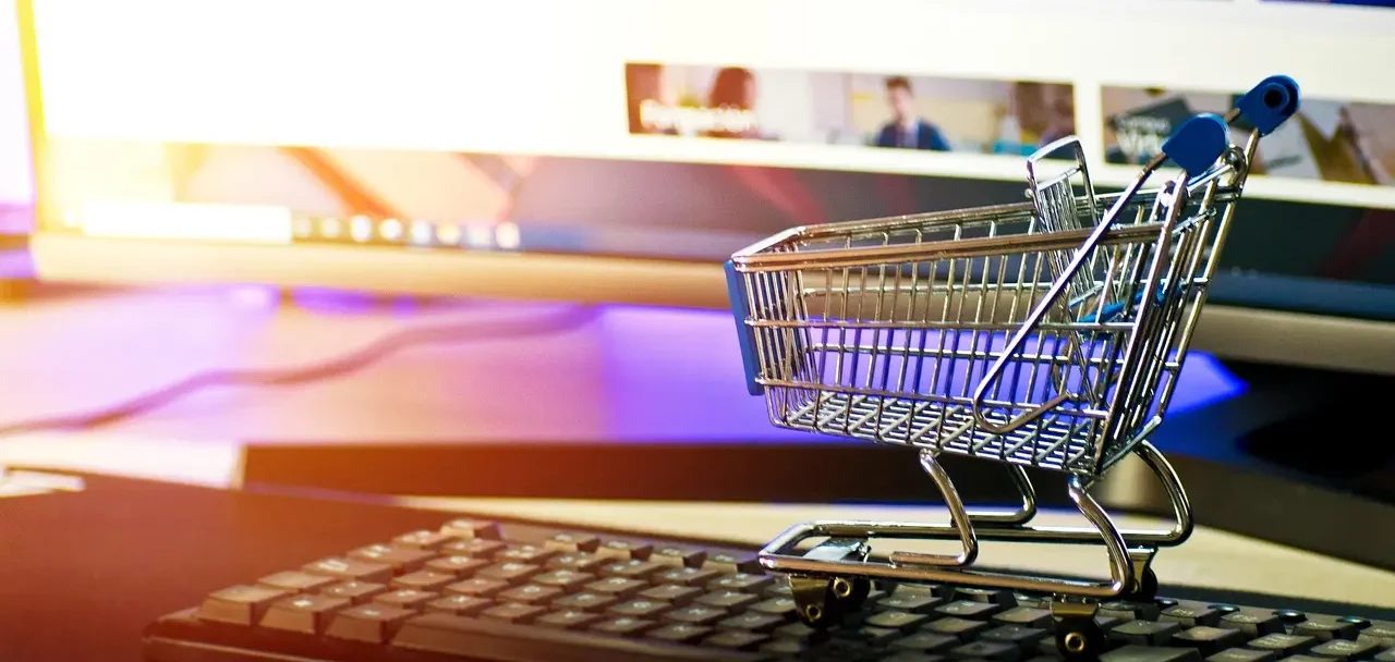 Imagem de um carrinho de compras em miniatura apoiado sobre um teclado de computador