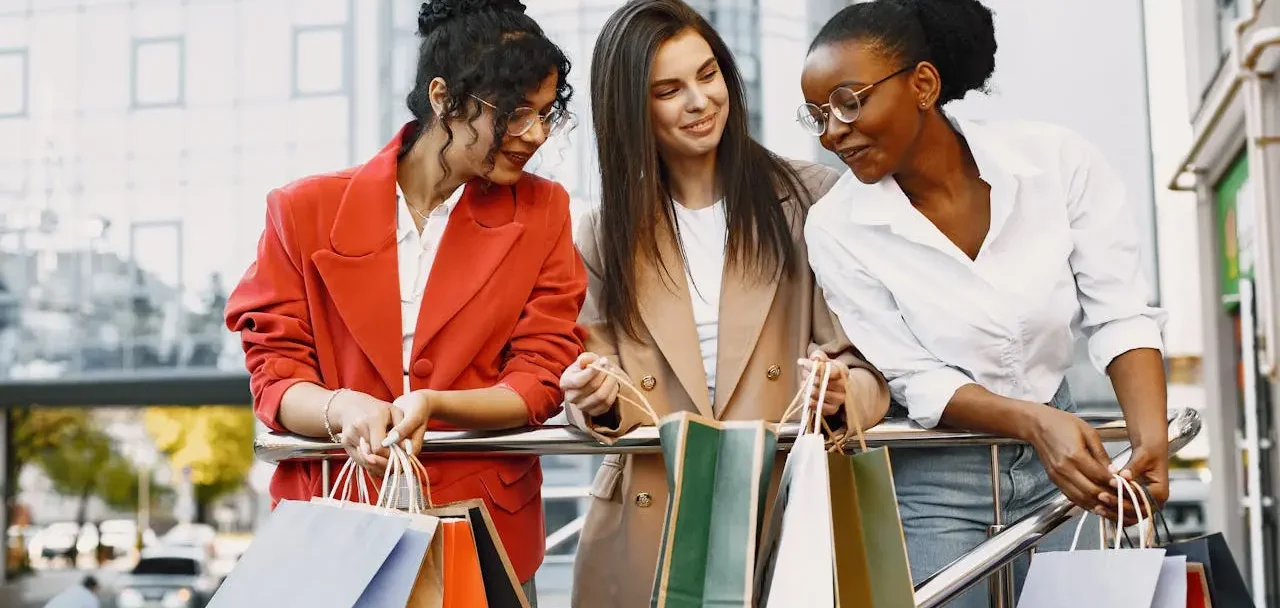 Imagem mostras três mulheres sorridentes com várias sacolas de compras nas mãos