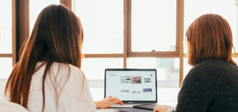 Duas pessoas analisando o design de um site em um notebook durante uma reunião.