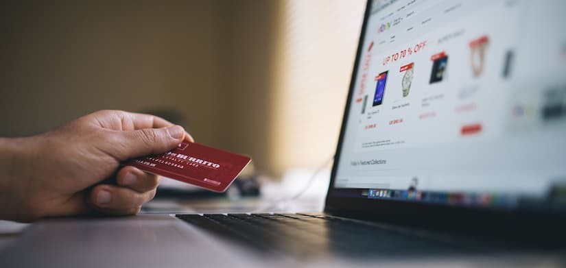 Pessoa segurando cartão de crédito em frente a notebook com loja virtual aberta.