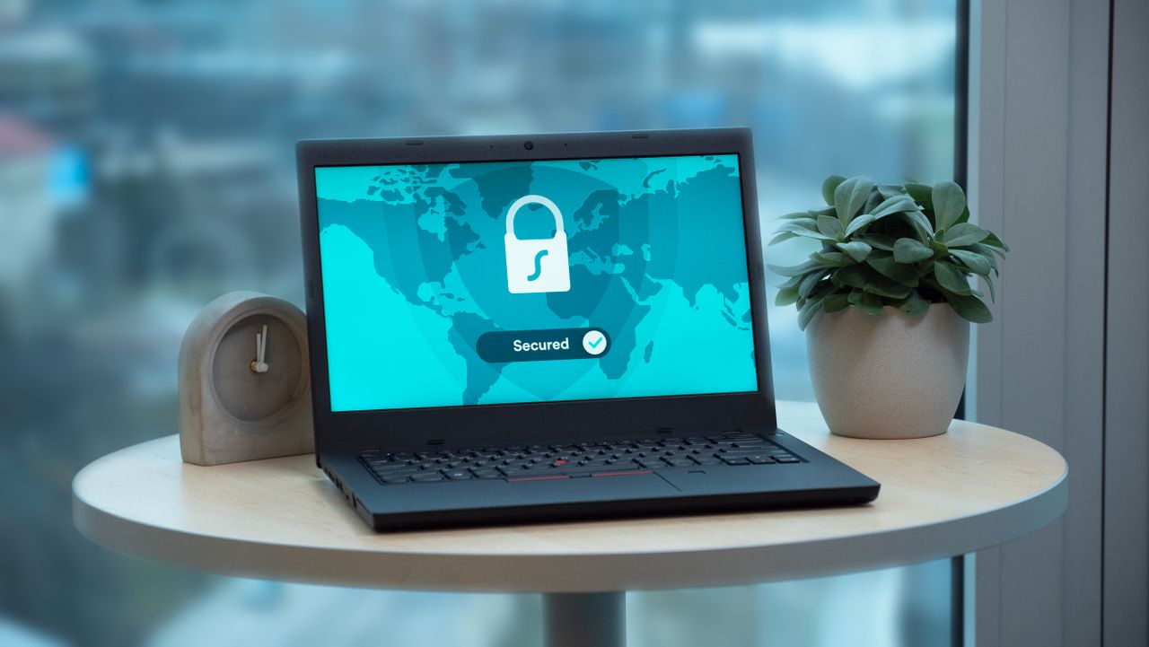 Imagem de um computador preto sobre uma mesa de madeira, exibindo umatela azul com o ícone de um cadeado e a palavra "Secured".